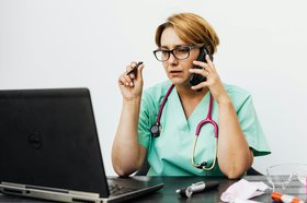 Eine Medizinerin sitzt mit Telefon und Stethoskop vor einem Computer. Foto: Karolina Grabowska/Pexels