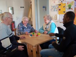 3 Frauen und ein Mann sitzen am Tisch und spielen Mensch-ärger-dich-nicht.
