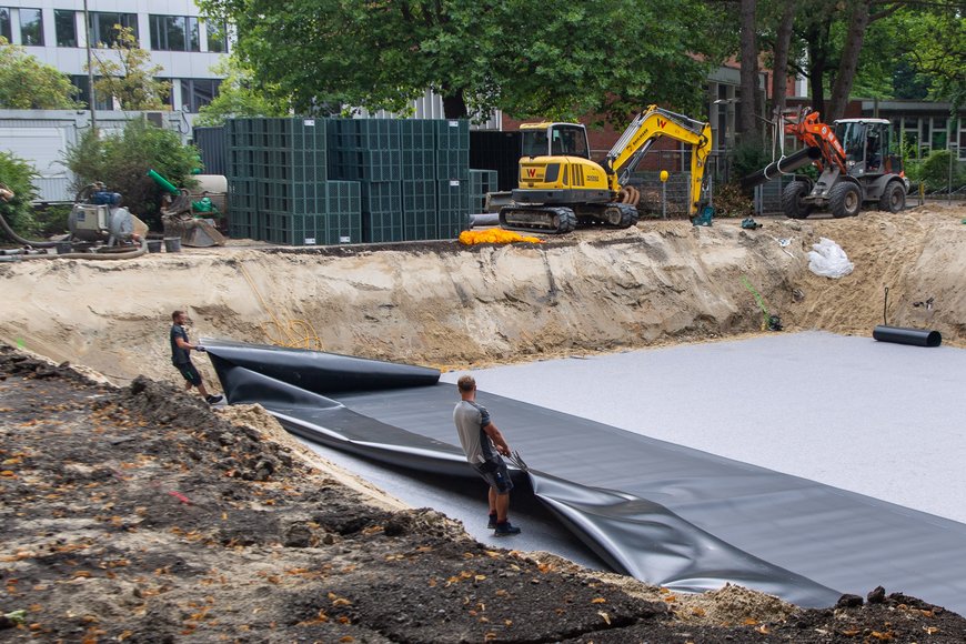 Die schwarze Folie wird in der Baugrube von zwei Bauarbeitern plaziert. Foto: Sascha Stüber