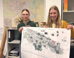 Janne und Paula mit einer großen Karte vor einem großen Plan der Stadt Oldenburg. Foto: Stadt Oldenburg