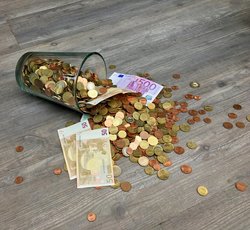 Münzen und Banknoten auf grauer Holzoberfläche verstreut.