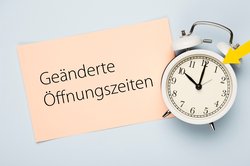 Eine analoge Uhr mit Hinweiszettel geänderte Öffnungszeiten